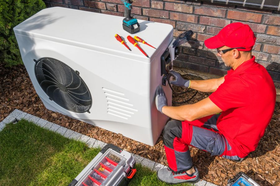 HVAC technician installing an outdoor AC unit beside a brick wall with tools nearby