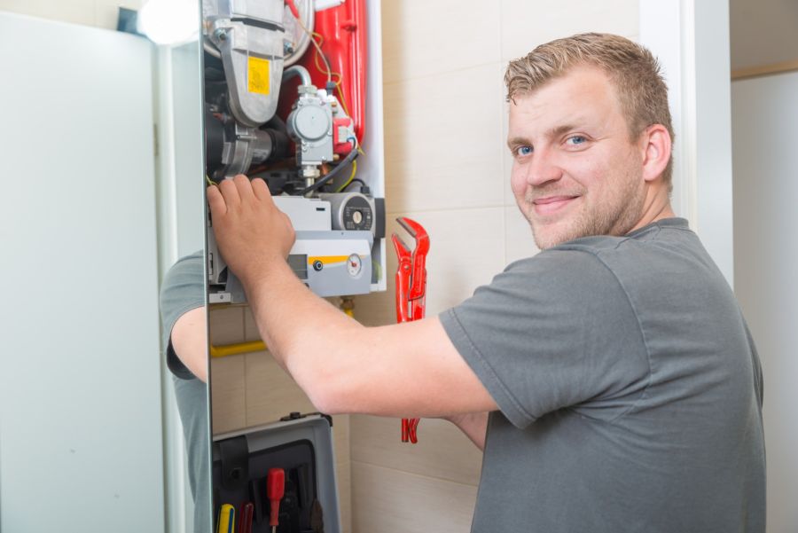 HVAC technician installing a furnace in a home utility room with open furnace panel and tools
